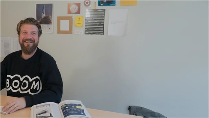 Foto: Kirchhoff: Mitarbeiter arbeitet fröhlich, neben ihm liegt ein aufgeschlagenes Buch