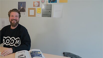 Photo: Kirchhoff: Employee working happily, with an open book lying next to him